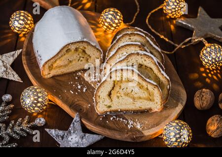 Weihnachtsstollen auf einem Holzbrett, Lichter und weihnachtsdekoration im Holzhintergrund, traditioneller deutscher weihnachtskuchen Stockfoto