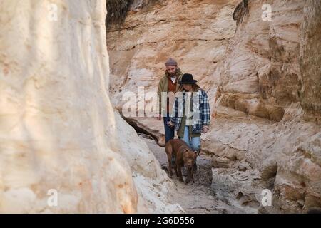 Junges Paar, das mit seinem Hund im Freien entlang der Felsen läuft Stockfoto