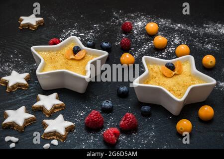 Creme Brulee: Traditionelles dessert aus französischer Vanillecreme mit karamellisiertem Zucker auf der Oberseite, serviert mit Beeren und weihnachtsplätzchen auf schwarzem Hintergrund Stockfoto