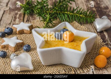 Creme Brulee: Traditionelles dessert aus französischer Vanillecreme mit karamellisiertem Zucker auf der Oberseite, serviert in sternförmiger Form mit weihnachtlicher Dekoration auf einer Woo Stockfoto