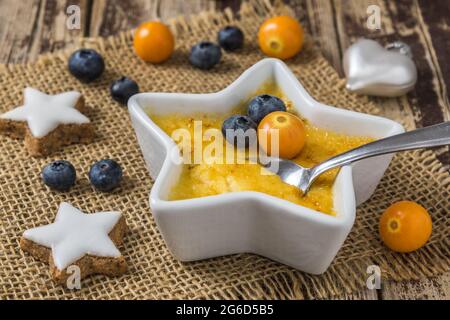 Creme Brulee: Traditionelles dessert aus französischer Vanillecreme mit karamellisiertem Zucker auf der Oberseite, serviert in sternförmiger Form mit weihnachtlicher Dekoration auf einer Woo Stockfoto