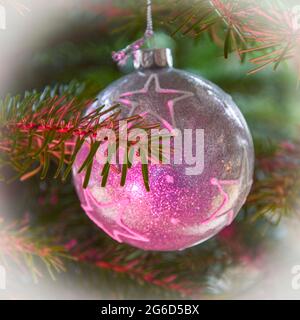 Schöne silberstrukturierte weihnachtskugel mit weißen Sternen an einer Tanne mit rosa Lichtreflexion, selektiver Fokus auf Tannenzweig Stockfoto