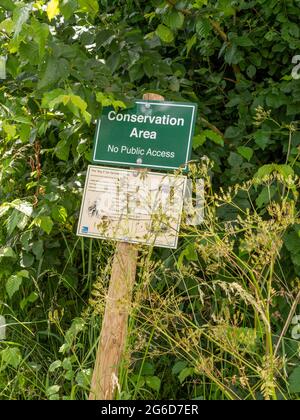 Ein grünes rechteckiges „Conservation Area“-Schild auf einem Holzpfosten in einer Hecke neben einem Feldgebiet Stockfoto