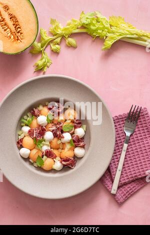 Von oben exotischer Melone, Mozzarella und Prosciutto-Salat auf rosa buntem Hintergrund Stockfoto