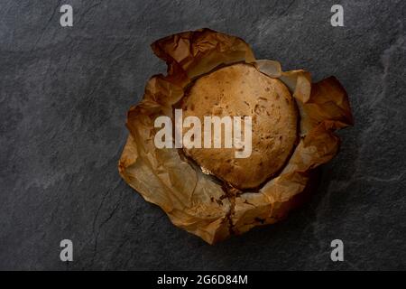 Draufsicht auf frisch gebackenes, handgemachtes, rundes Brot mit knuspriger Kruste auf Pergamentpapier auf schwarzem Hintergrund Stockfoto