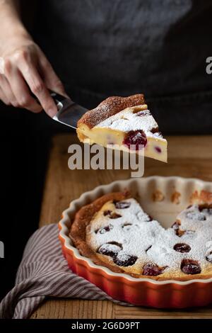 Gesichtslose Person, die am Tisch mit einem geschnittenen Stück leckeren Kuchen mit Kirschen steht Stockfoto