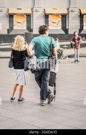 Verheiratetes Paar, das Straßenmusiker beobachtet und fotografiert, Blick von hinten. Regelmäßige Menschen auf öffentlichen Plätzen Stockfoto