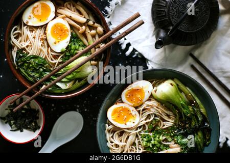 Draufsicht auf Keramikschüsseln mit köstlichem Ramen und Essstäbchen auf dem Tisch Stockfoto