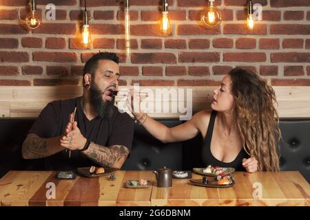 Liebende Paare essen appetitliches Sushi, während sie an einem Holztisch im japanischen Restaurant sitzen Stockfoto
