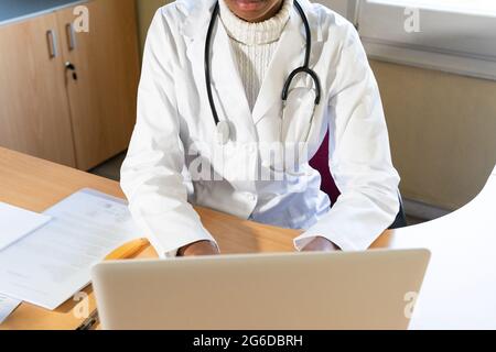 Von oben Ernte afroamerikanische Ärztin Eingabe Bericht auf Laptop während der Arbeit am Tisch in modernen Klinik Büro Stockfoto