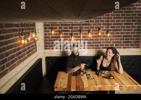 Liebende Paare essen appetitliches Sushi, während sie an einem Holztisch im japanischen Restaurant sitzen Stockfoto