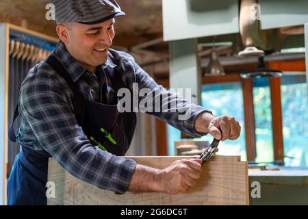 Fröhlicher männlicher Tischler glättende Holzdiele mit professioneller Holzbearbeitungsklinge spokeshave manueller Hobel in der Werkstatt Stockfoto