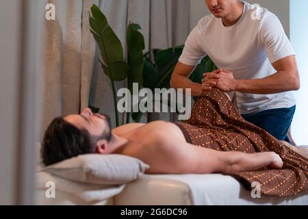 Seitenansicht eines anonymen Masseurs, der eine Thai-Massage für männliche Gäste im modernen Spa-Salon macht Stockfoto