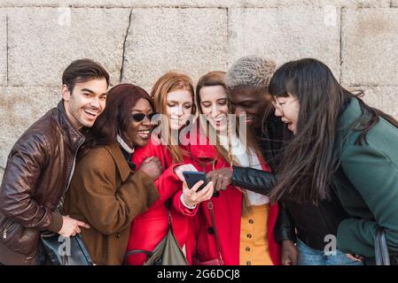 Gesellschaft von multiethnischen stilvollen Freunden, die sich auf der Straße treffen und zusammen lustige Videos auf dem Mobiltelefon ansehen Stockfoto