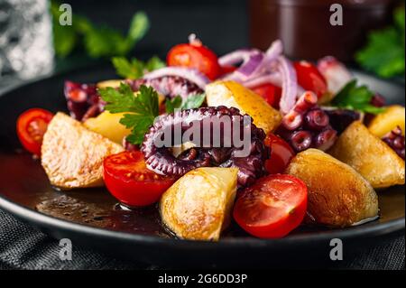 Leckerer Salat mit Oktopus und verschiedenen Gemüse- und Kräutersorten auf dem Tisch Stockfoto