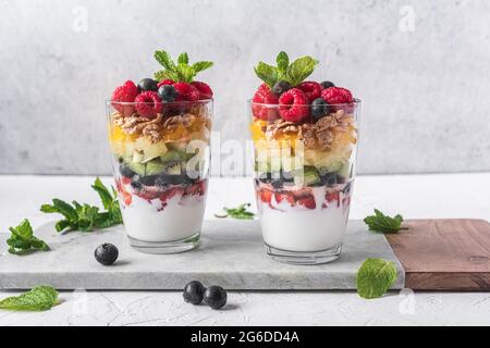 Appetitliches Joghurt mit Schichten von frischem Obst serviert in Gläsern auf dem Tisch mit Minzblättern Stockfoto