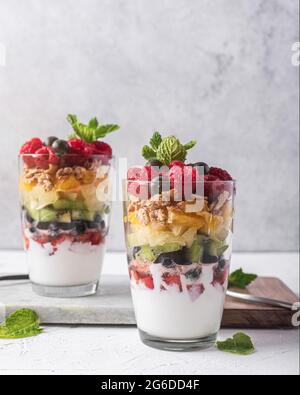 Appetitliches Joghurt mit Schichten von frischem Obst serviert in Gläsern auf dem Tisch mit Minzblättern Stockfoto