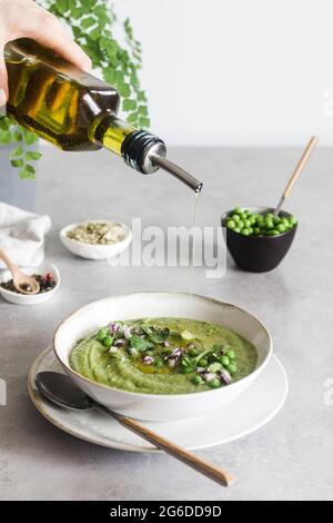 Anonyme Person gießt Olivenöl über köstliche Erbsen-Creme über Beton weißen Tisch Stockfoto