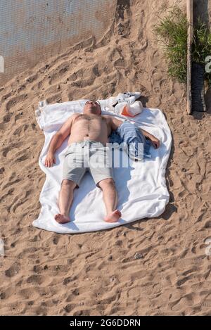 Sankt Petersburg, Russland - 20. Juni 2021: Ein Mann sonnenbaden auf einem Handtuch am Strand des Parks des 300. Jahrestages von Sankt Petersburg. Stockfoto