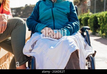 Crop unkenntlich weibliche Betreuerin sitzt mit älteren Frau im Rollstuhl an sonnigen Tag Stockfoto