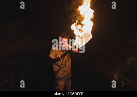 Junger männlicher Höhlenforscher mit brennender Fackel, der in einer dunklen, engen Felsenhöhle steht, während er die unterirdische Umgebung erkundet Stockfoto