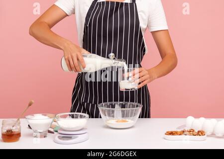 Zugeschnittenes Bild einer Konditorin oder Bäckerin, die Teig für Kuchen oder Kekse macht, gießt Milch ins Glas, um Mehl, hausgemachtes Gebäck hinzuzufügen. Stehbolzen für den Innenbereich Stockfoto