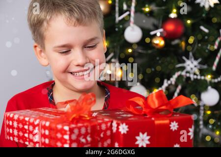 Happy Smiling Child mit Weihnachtsgeschenkschachteln in der Nähe von Christmas Tree. Weihnachts- und Neujahrsferien-Konzept Stockfoto