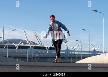 Lässiger Skater Mann auf Longboard im urbanen Raum. Hipster in modischer Street-Fashion-Kleidung Stockfoto