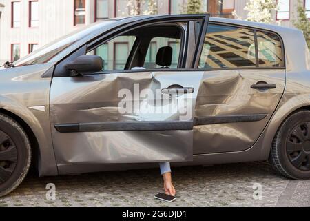 Unbekannte betrunkene Person, die in einem beschädigten Auto sitzt und schläft, Hände mit Telefon, Verkehrsverletzung durch betrunkenes Fahren, abgestürzte Autoteile nach gem Stockfoto