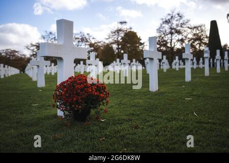 Nahaufnahme von weißen Kreuzen auf dem Gras auf dem Friedhof mit einem Blumenstrauß davor Stockfoto
