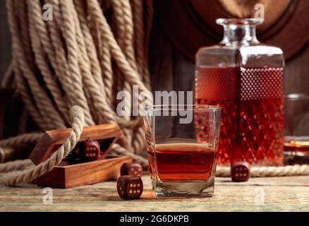 Starker Alkoholiker und Würfel auf einem alten Holztisch. Im Hintergrund sind ein Hanfseil und ein Männerhut. Stockfoto