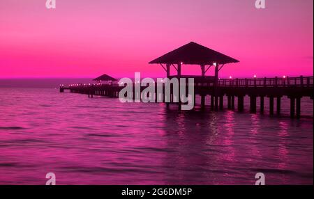 Die Silhouette eines hölzernen Pavillons im Pop-Art-Stil am Pier bei Sonnenuntergang in lebhaftem, violettem Pink Stockfoto