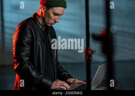 Moderner Hacker in schwarzer Lederjacke mit Laptop Stockfoto