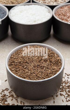 Kümmel. Becher mit Kümmel auf einem Hintergrund verschiedener Samen in schwarzen Behältern auf einer Marmorplatte. Stockfoto