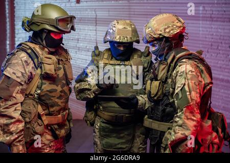 Drei Männer in militärischem Outfit, die Tablets benutzen, um Kriminelle zu finden Stockfoto