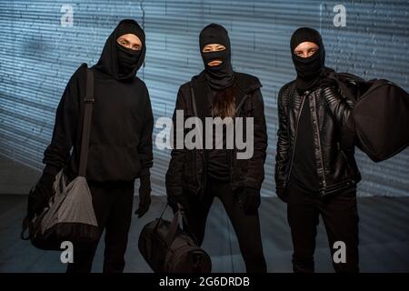 Drei Diebe in schwarzem Outfit mit Handtaschen und gestohlenen Sachen Stockfoto