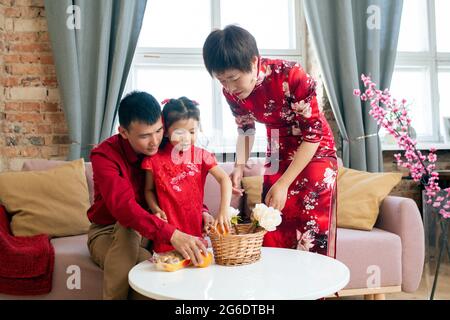Chinesische Familie sitzt am Tisch im Wohnzimmer, während sie zu einem Snack geht Stockfoto
