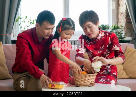 Kleines chinesisches Mädchen in rotem Kleid hilft Eltern Snack in den Korb zu legen Stockfoto