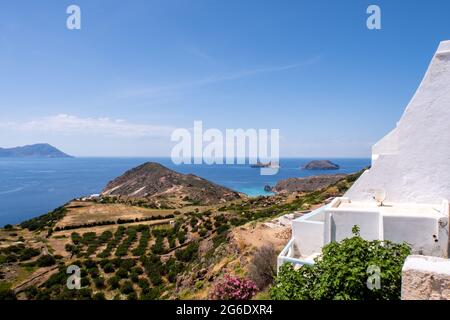 Blick auf das Meer von Plaka Town auf der Insel Milos, Griechenland, mit weiß getünchten traditionellen Häusern und grünen Weinbergen im Vordergrund und kristallklarem Himmel. Stockfoto