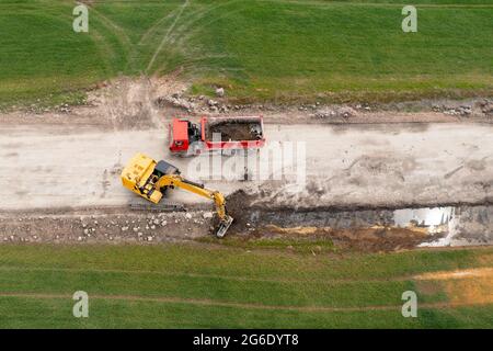 Bagger graben Boden in der Nähe des Feldes und Verladung auf den LKW Stockfoto
