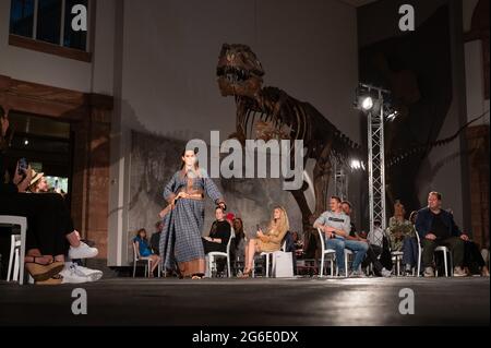 05. Juli 2021, Hessen, Frankfurt/M.: Während der Modenschau des Designers Samuel Gärtner im Senckenberg Museum läuft ein Modell vor dem Skelett eines Tyrannosaurus. Die Modenschau findet zu Beginn der Frankfurter Fashion Week statt, die vom 5. Bis 9. Juli stattfindet. Es ist jedoch nicht Teil des offiziellen Programms. Foto: Sebastian Gollnow/dpa Stockfoto