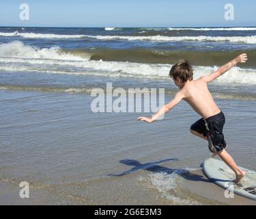 Kleiner Junge auf einem Boogie Board, der sich im Sommer mit seinen Armen am Rand des Ozeans balanciert. Stockfoto