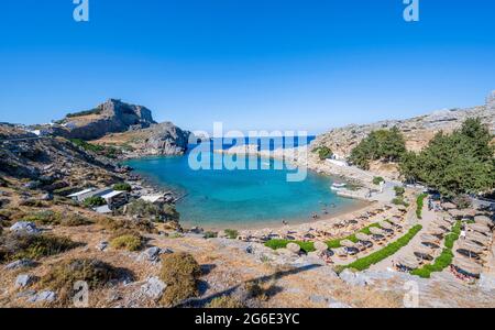 Paulus Bay, Strand mit Sonnenliegen und Sonnenschirmen, hinter der Akropolis von Lindos, Lindos, Rhodos, Doedekanes, Griechenland Stockfoto