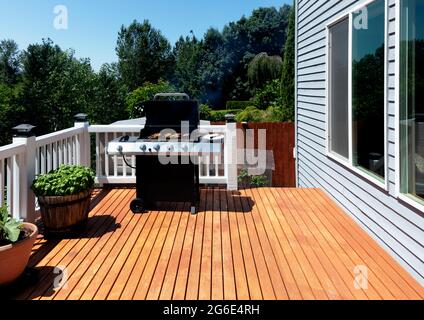 BBQ-Herd im Freien mit offenem Deckel, der im Sommer auf der Holzterrasse des Hauses Rauch ausgibt Stockfoto