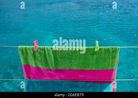 Strandtuch trocknen auf Wäscheleine, verwischen Meereshintergrund. Buntes Handtuch, das an der Edelstahlschiene des Bootes hängt. Sommerferien und Segeln, Wäsche waschen und Stockfoto