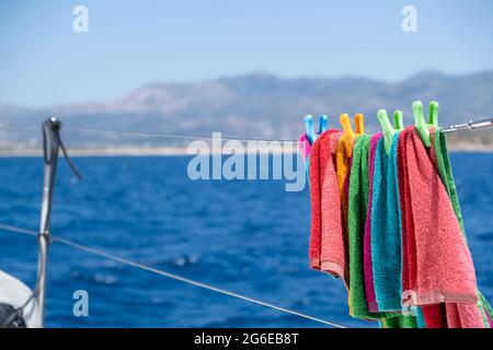 Strandtuch trocknen auf Wäscheleine, verwischen Meereshintergrund. Buntes Handtuch, das an der Edelstahlschiene des Bootes hängt. Sommerferien und Segeln, Wäsche waschen und Stockfoto