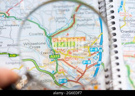 Nahaufnahme einer Seite in einem gedruckten Straßenkarte-Atlas mit einer Männerhand, die eine Lupe hält, die eine Vergrößerung der Stadt in Exeter, England, zeigt Stockfoto