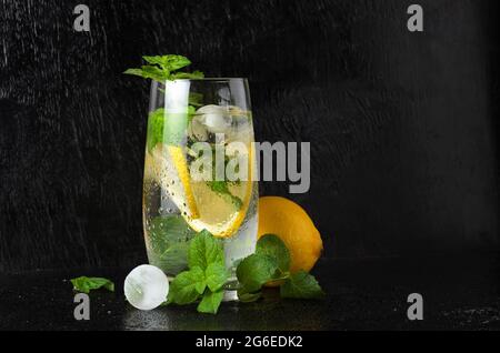 Ein großes Glas Wasser mit Zitrone, Minzblättern und Eis, bedeckt mit Wassertropfen. Ein Glas Limonade auf einem schwarzen strukturierten Hintergrund. Selektiver FOC Stockfoto