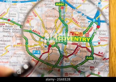 Nahaufnahme einer Seite in einem gedruckten Straßenkarte-Atlas mit einer Männerhand, die eine Lupe mit einer Vergrößerung der Stadt Coventry in England hält Stockfoto