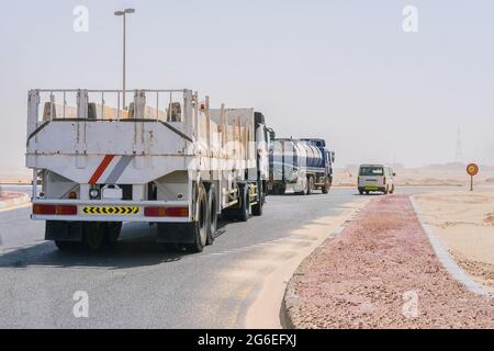 Gruppe von LKW-Transporten, Lieferwagen und Tankwagen, auf der Autobahn durch die Wüste mit verschwommenen Sanddünen im Hintergrund durch Sandsturm. Stockfoto